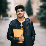 handsome young indian student man holding notebooks while standing on the street
